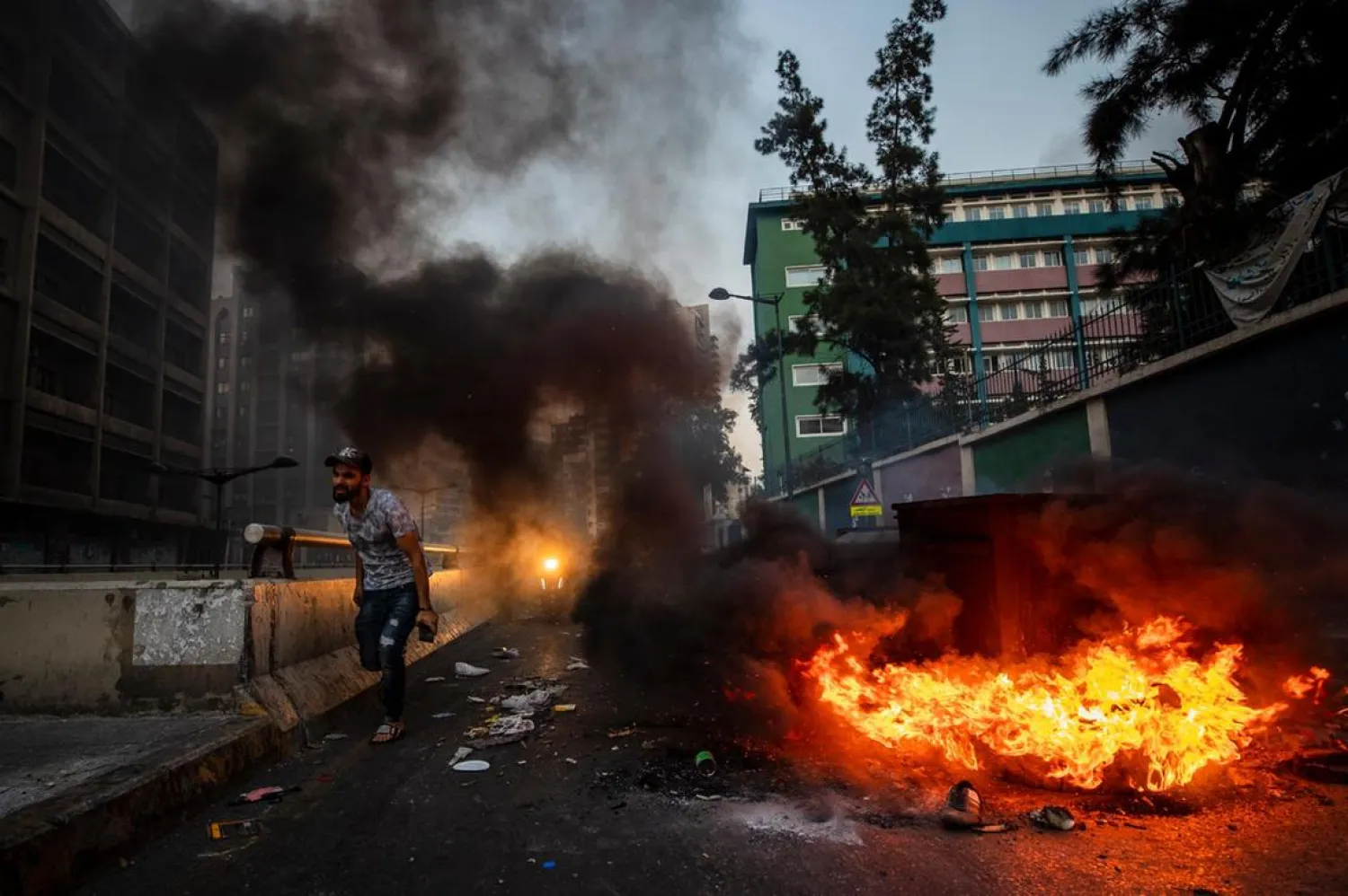 People pass garbage containers and tires that were set on fire by anti-government protesters to block the main road in Beirut, Lebanon. (AP)