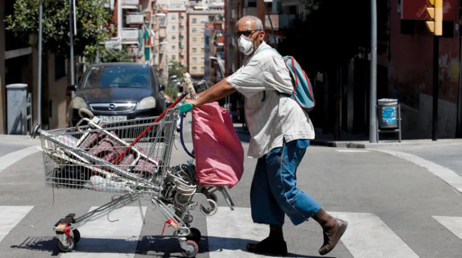 رجل يدفع عربة تسوّق في منطقة توراسا قرب برشلونة أمس (إ.ب.أ)