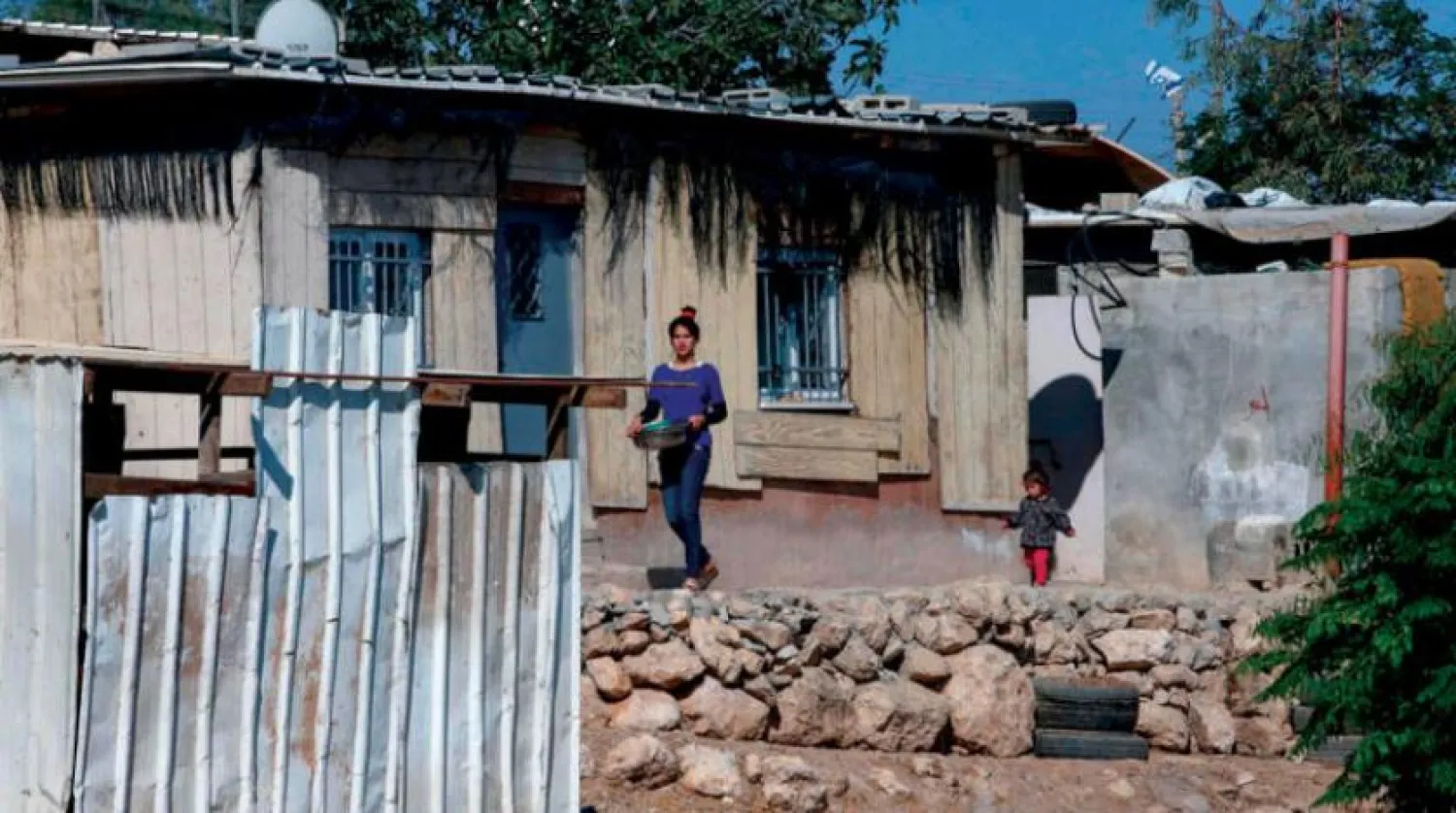 عائلة في قرية الاسيفر في الضفة... وخلف المنزل علم إسرائيلي على مستوطنة ياتير (أ.ف.ب)
