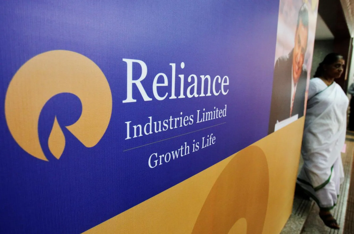 FILE PHOTO: A woman walks past a poster of Reliance Industries installed outside the venue of the company's annual general meeting in Mumbai June 7, 2012. REUTERS/Vivek Prakash/File Photo