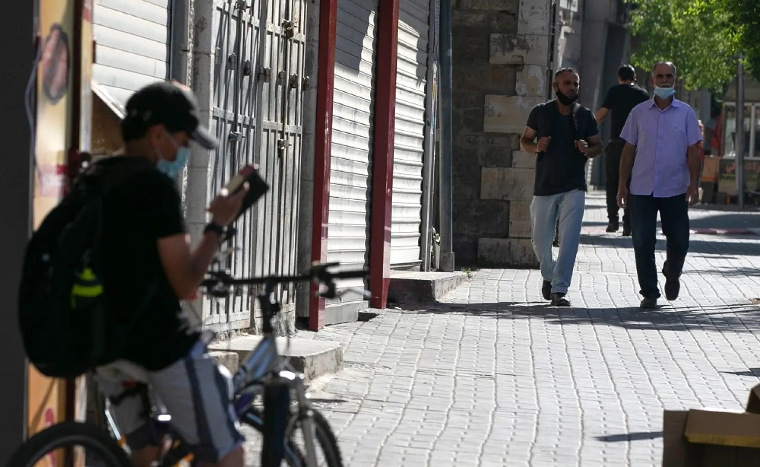 Palestinian men walk in front of closed shops in the occupied West Bank city of Ramallah, on July 13, 2020, amid the coronavirus pandemic crisis. (AFP)
