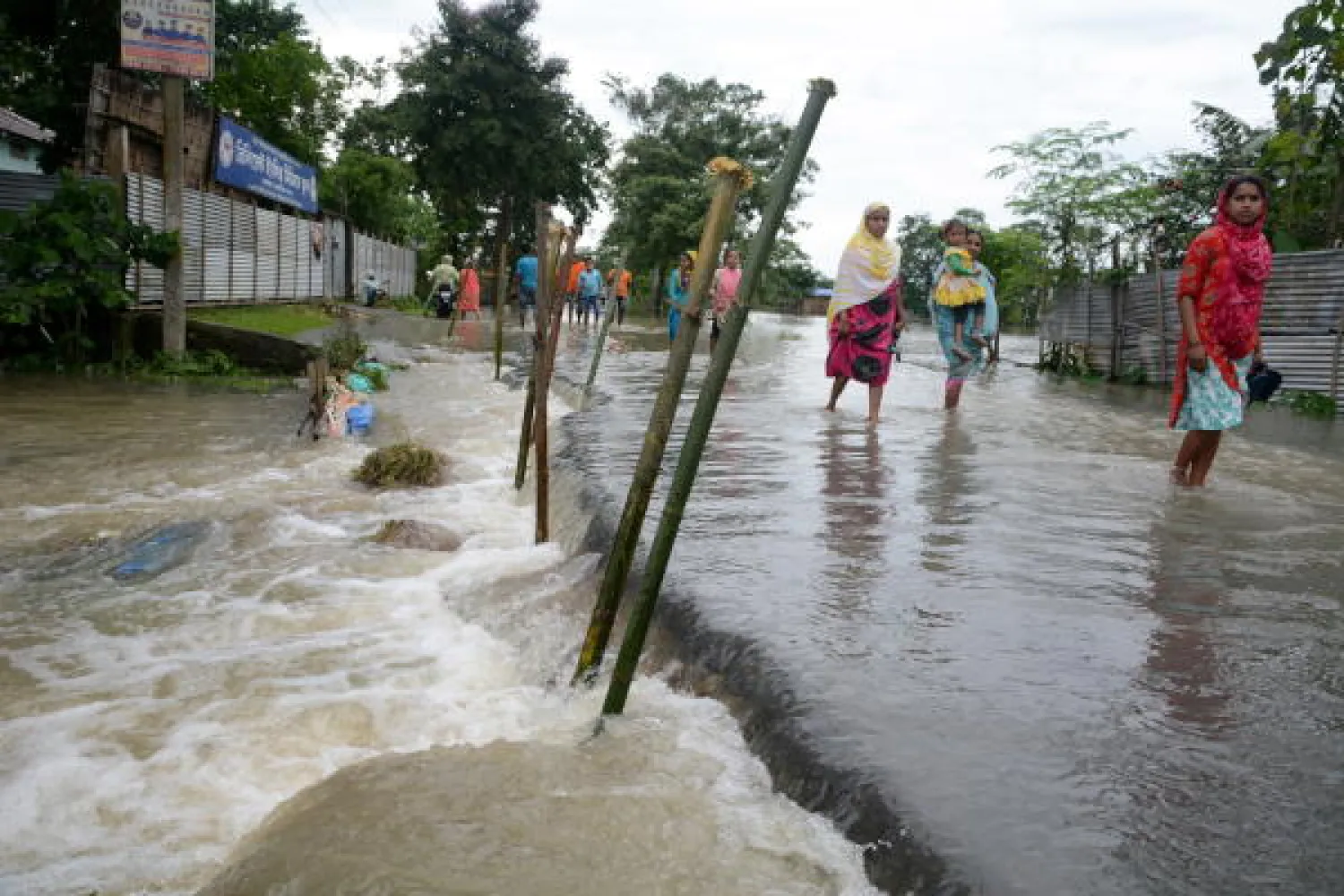 Indian people wade through a flooded street as a part of the road is washed away at Chamata in Nalbari district of Assam, India, 27 May 2020. Flood water has risen in at least seven districts of Assam state after the water level continued to rise in Brahmaputra river, following incessant rains over the last few days. EPA/STR