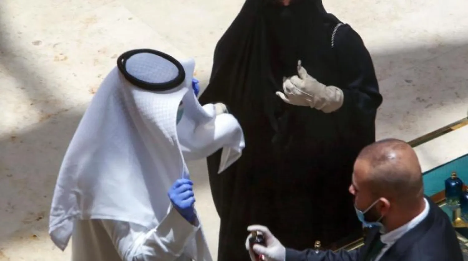 Görevlilerden biri Kuveyt’teki akışveriş merkezine gelen ziyaretçiye dezenfektan püskürtürken (AFP)