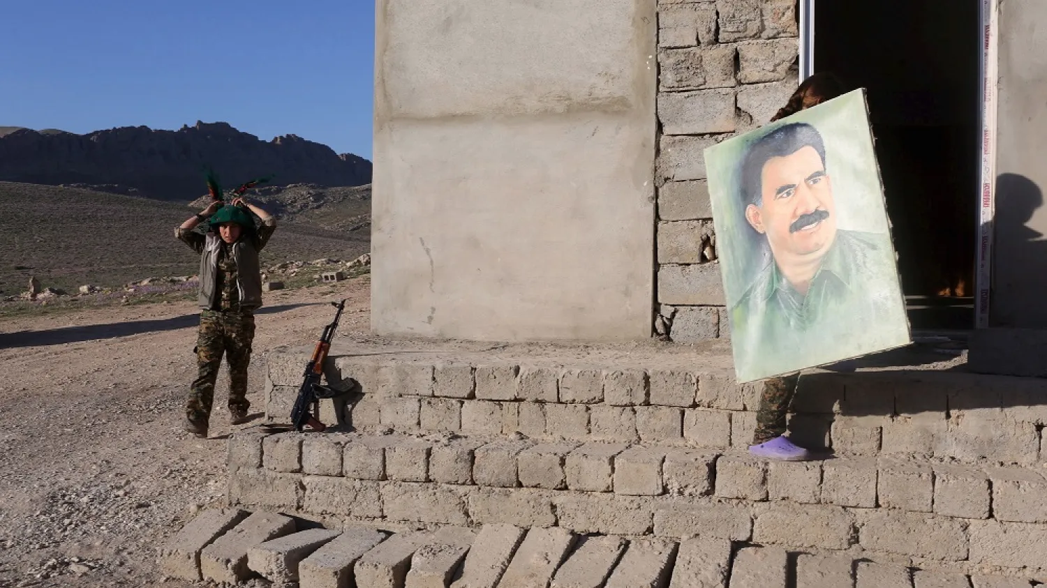 A female PKK fighter adjusts her scarf while another carries a picture of jailed Kurdish leader Abdullah Ocalan at their base in Sinjar March 11, 2015. (Reuters)