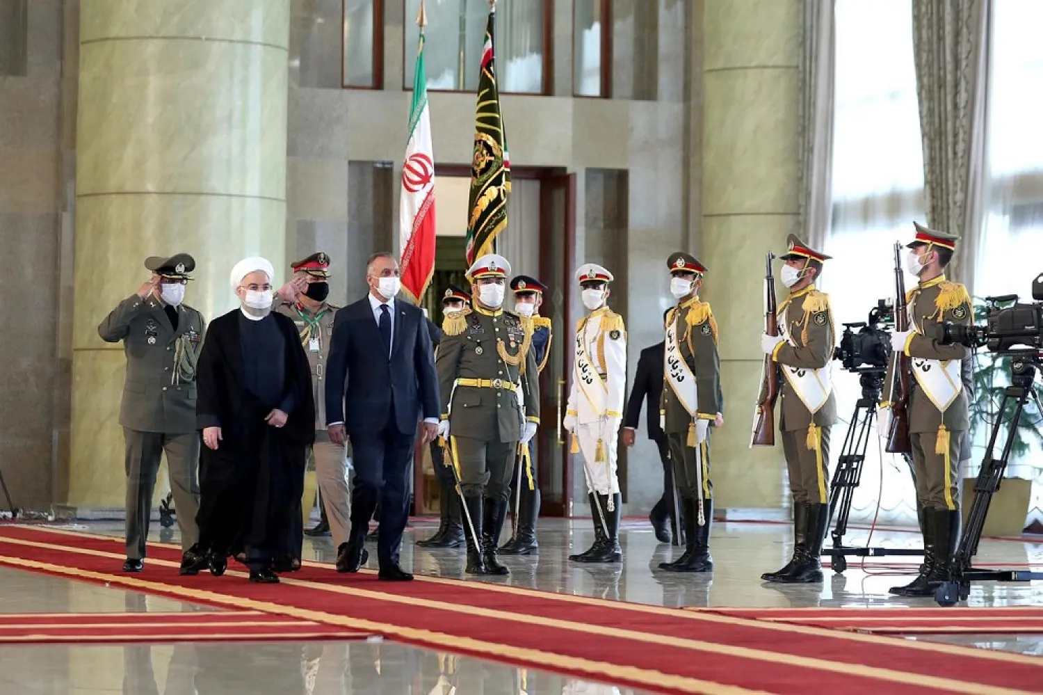 Iranian President Hassan Rouhani and Iraqi Prime Minister Mustafa al-Kadhimi walk during a welcome ceremony, as they wear protective masks, in Tehran, Iran, July 21 2020. (Handout via Reuters)
