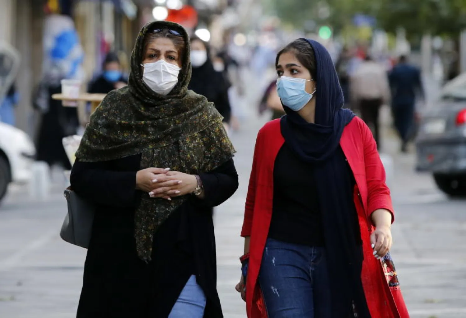 سيدتان إيرانيتان ترتديان قناعي وجه تسيران في شارع بالعاصمة طهران (إ.ب.أ)