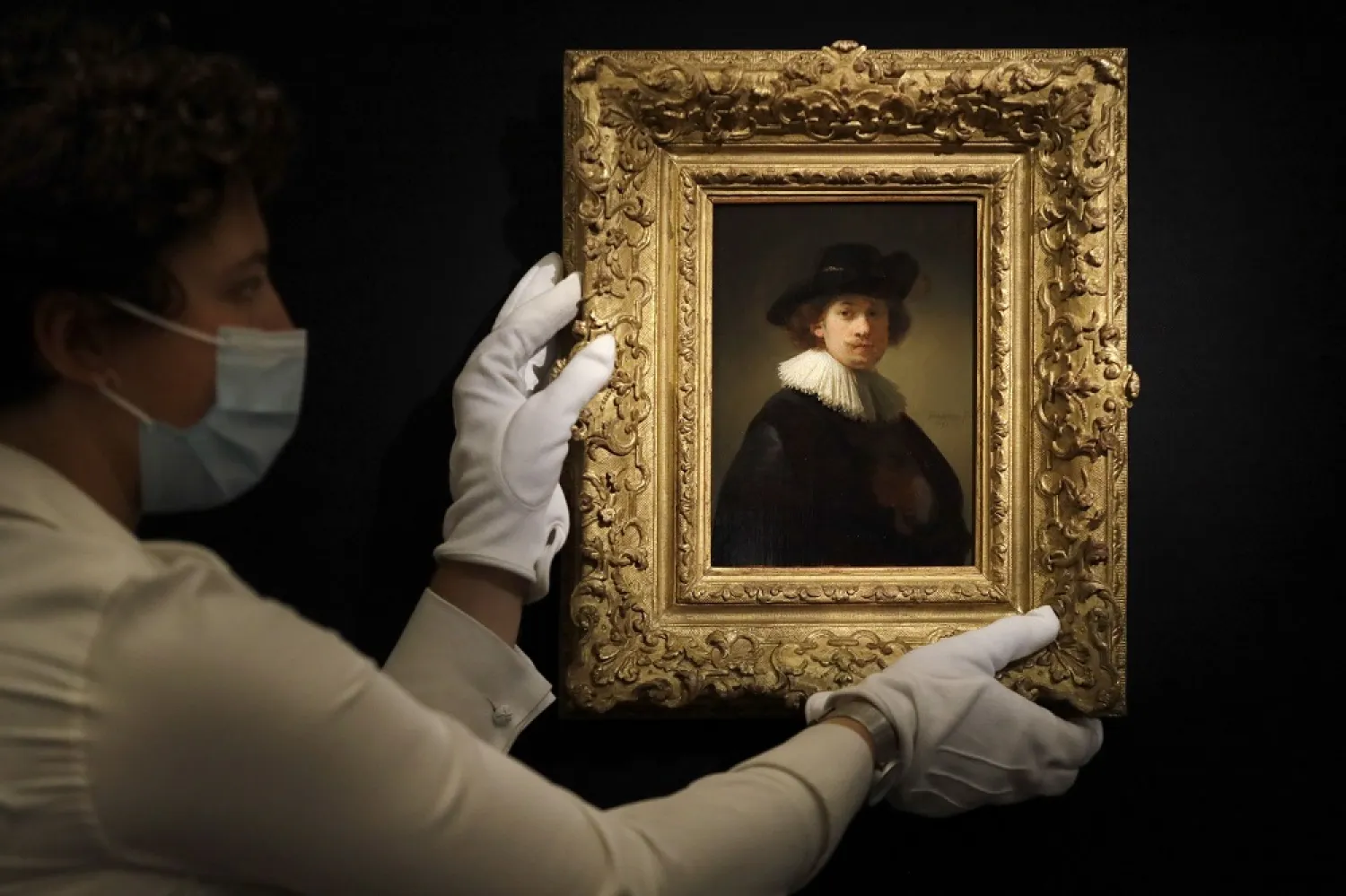 In this July 23, 2020 photo, a Sotheby's employee adjusts a painting by Rembrandt, entitled 'Self-portrait, wearing a ruff and black hat' at Sotheby's auction rooms in London. (AP)