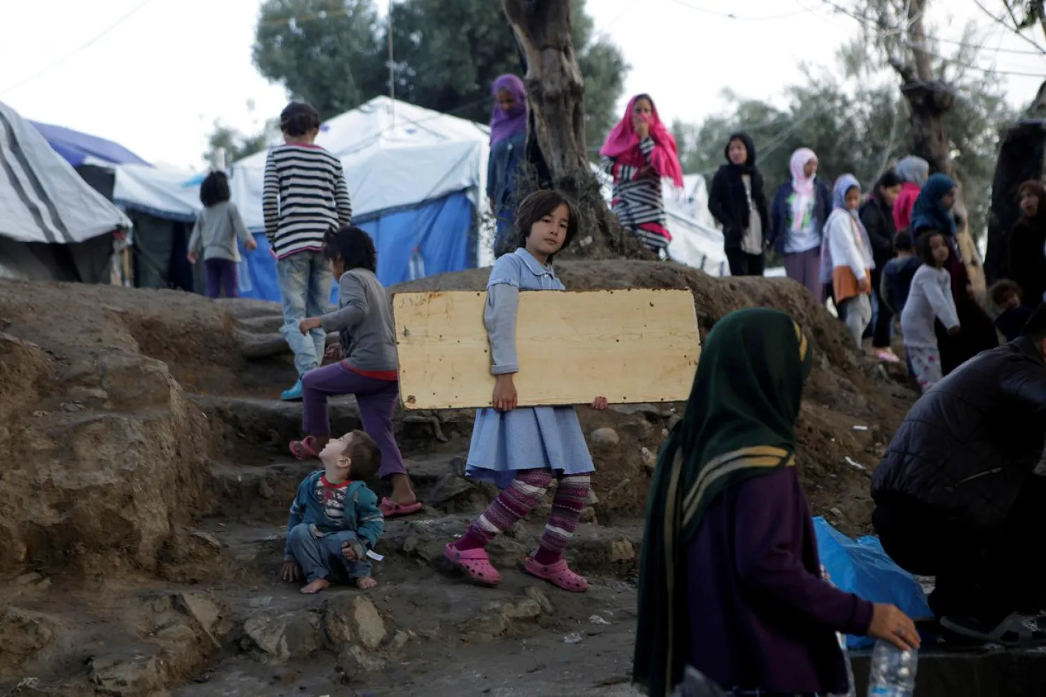 FILE PHOTO: A girl carries a wooden board as she makes her way at a makeshift camp for refugees and migrants next to the Moria camp, on the island of Lesbos, Greece, November 15, 2019. REUTERS/Elias Marcou/