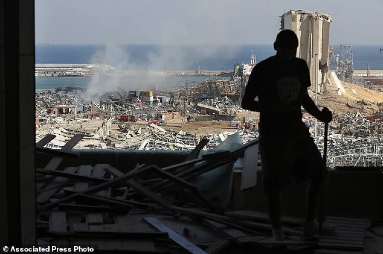 A man stands in a damaged apartment as he looks out at the scene of a massive explosion that hit the seaport of Beirut, Lebanon, Wednesday, Aug. 5, 2020. Residents of Beirut awoke to a scene of utter devastation on Wednesday, a day after a massive explosion at the port sent shock waves across the Lebanese capital, killing at least 100 people and wounding thousands. (AP Photo/Hussein Malla)