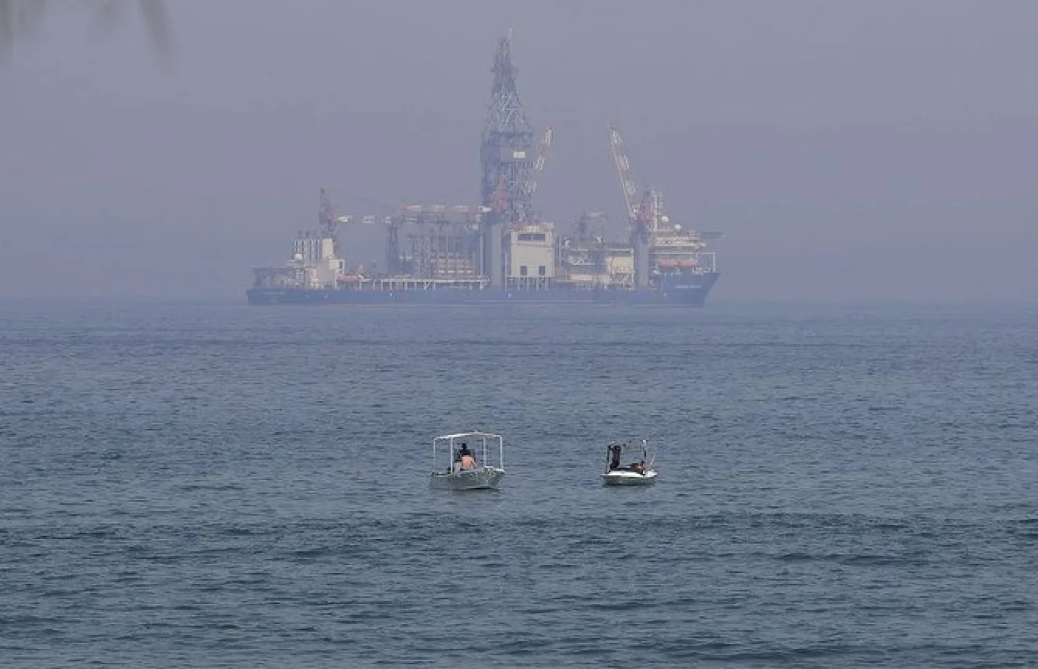 Lebanese people sit in boats in the Mediterranean sea as the Tungsten Explorer, a drillship to explore for oil and gas off the coast of Lebanon, is seen in the background in Dbayeh north of the capital Beirut. (File/AFP)

