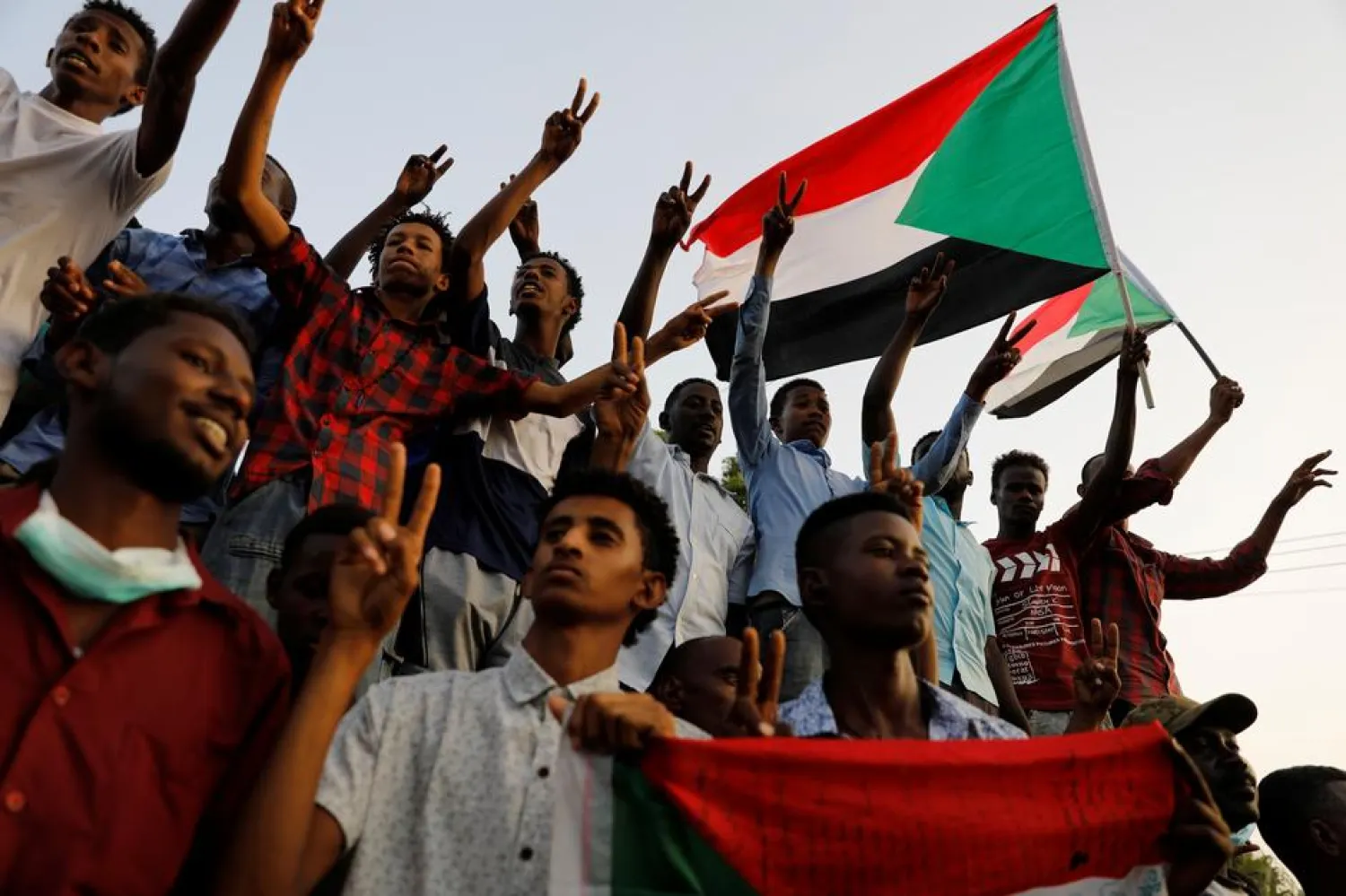 Sudanese demonstrators make victory signs and wave Sudanese flags as they protest in front of the Defence Ministry in Khartoum, Sudan (Reuters)

