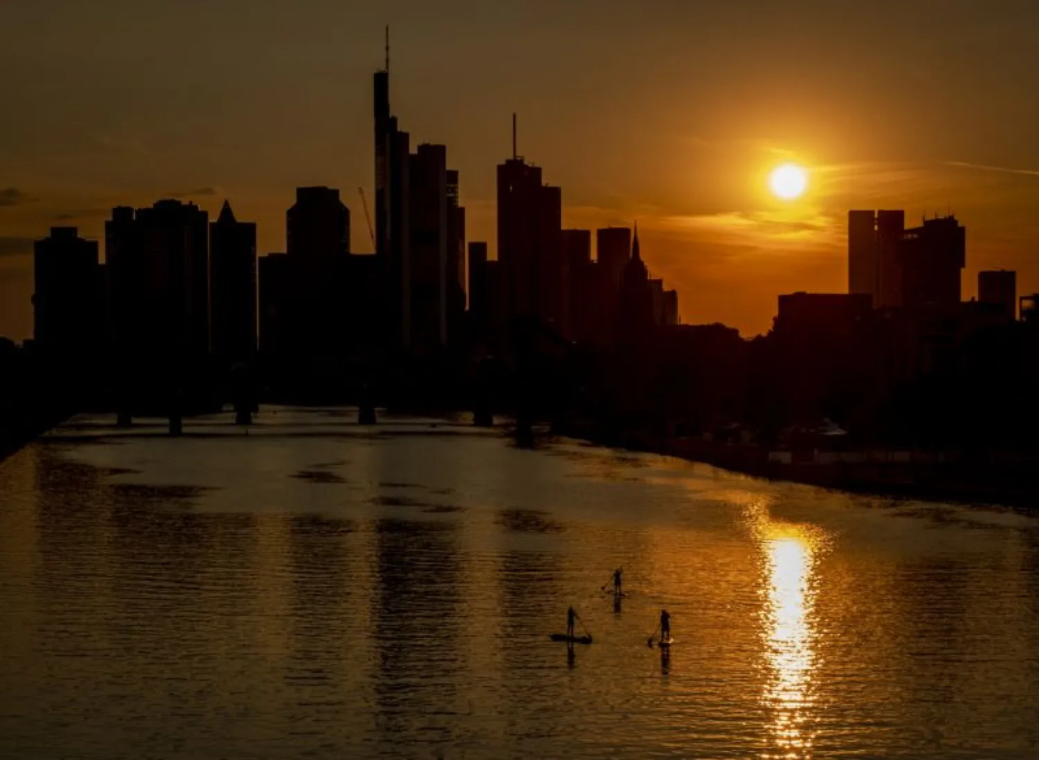 Three stand up paddlers on the river Main in Frankfurt, Germany, as the sun sets, Tuesday, Aug. 4, 2020. (AP Photo/Michael Probst)
