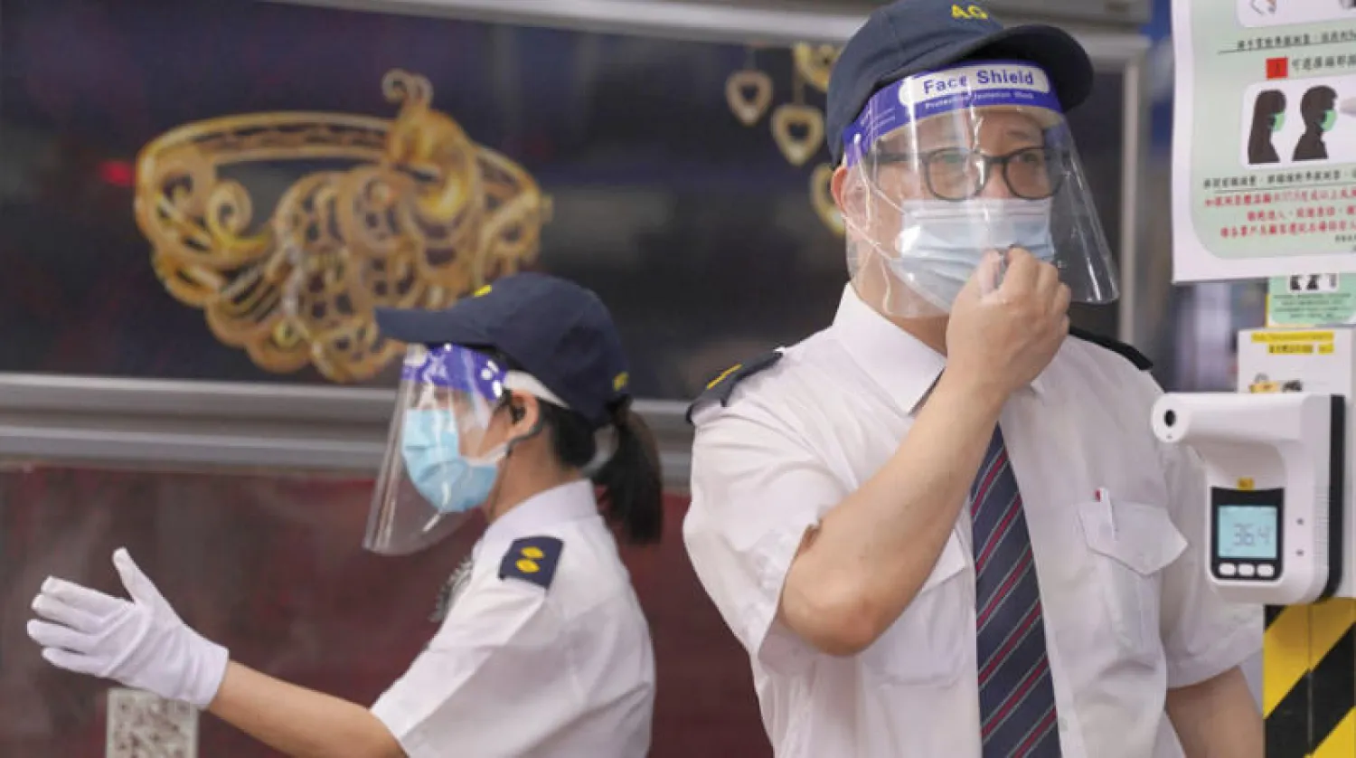 حارسان يفحصان حرارة زوار مركز تسوق في هونغ كونغ أمس (رويترز)