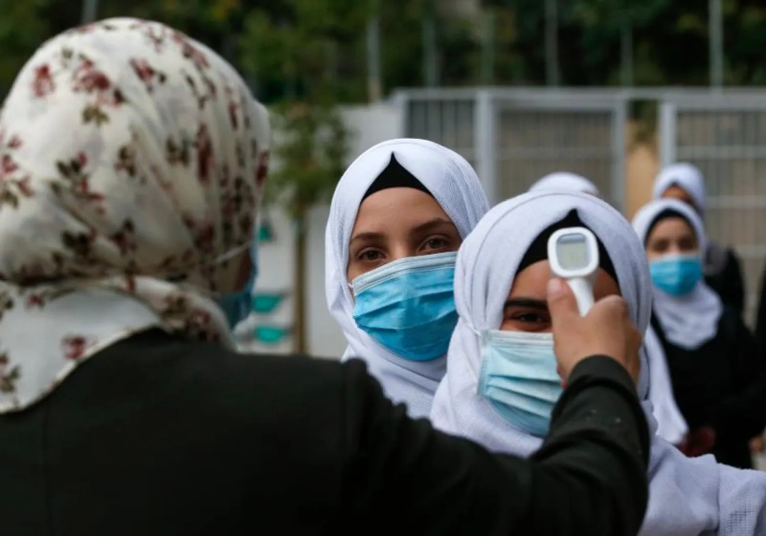 عاملة صحية تقيس حرارة طالبات قبل دخولهن مدرسة في الخليل (رويترز)