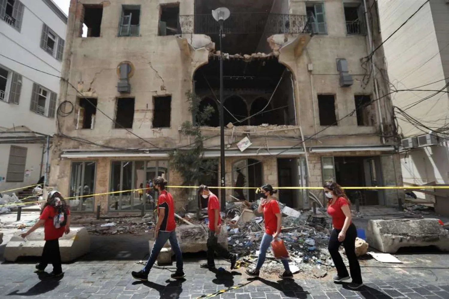 University students who volunteered to help clean damaged homes and give other assistance, pass in front of a building that was damaged by last week's explosion, in Beirut, Lebanon, Tuesday, Aug. 11, 2020. The explosion that tore through Beirut left around a quarter of a million people with homes unfit to live in. But there are no collective shelters, or people sleeping in public parks. That's because in the absence of the state, residents of Beirut opened their homes to relatives, friends and neighbors. (AP Photo/Hussein Malla)
