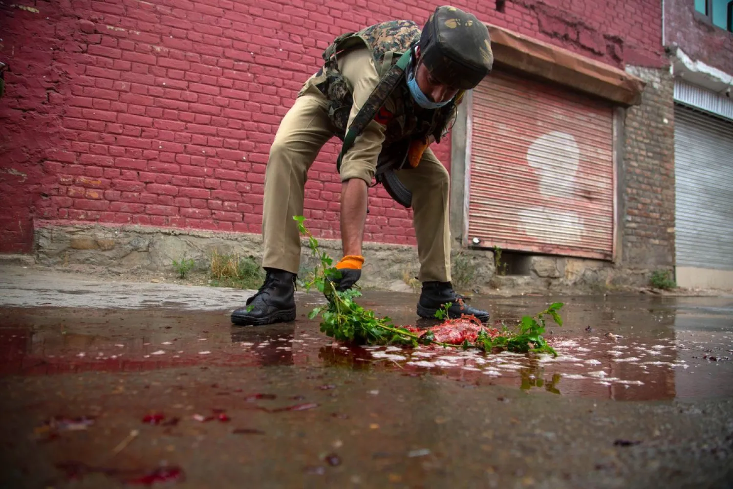 An Indian policeman cleans blood splattered on a street with a tree twig after suspected rebels attack on policemen on the outskirts of Srinagar, Indian controlled Kashmir, Friday, Aug. 14, 2020. Anti-India rebels in Indian-controlled Kashmir Friday attacked a police party in the disputed region's main city, killing two police officials and injuring another, police said. (AP Photo/Mukhtar Khan)