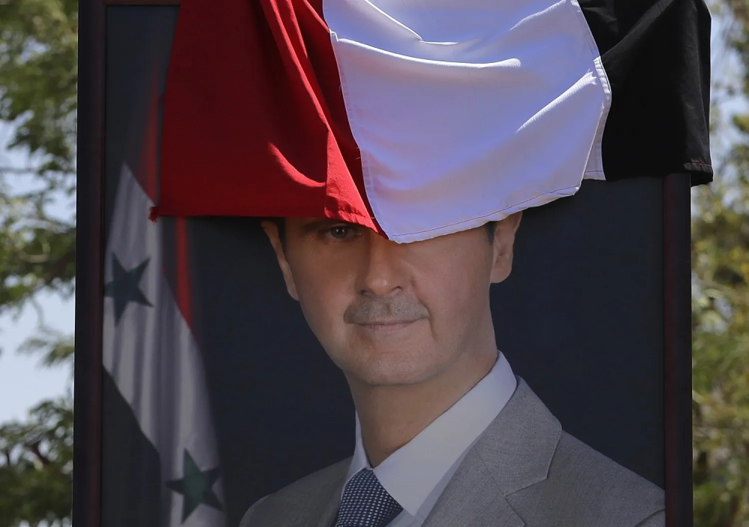 In this Aug. 13, 2018 file photo, a poster of Syrian president Bashar Assad, half-covered by a national flag, hangs at the border crossing point of Jdedeh Yabous, Syria. (AP)