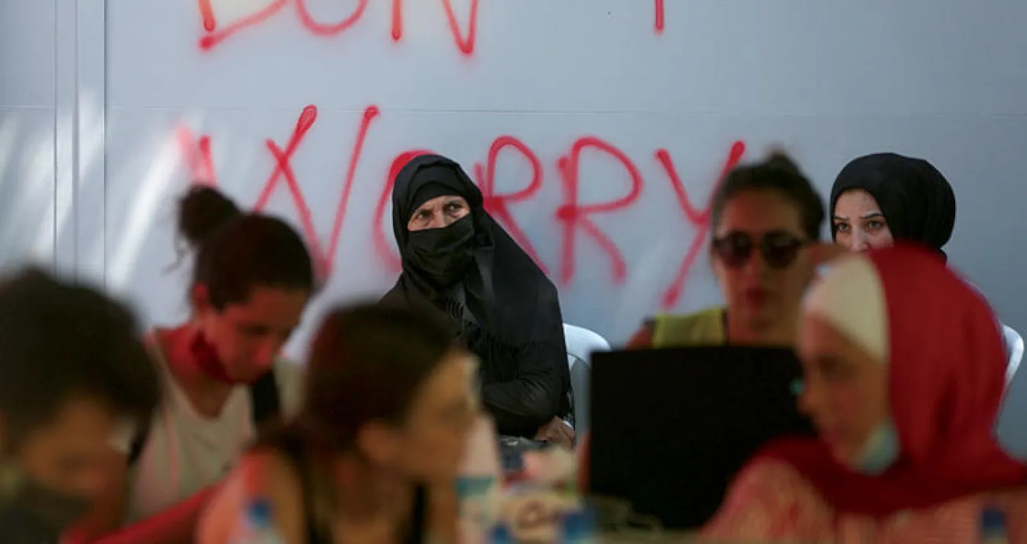 متطوعون يساعدون امرأة متضررة من التفجير تجلس أمام حائط كُتب عليه «لا تقلقوا» (أ.ف.ب)