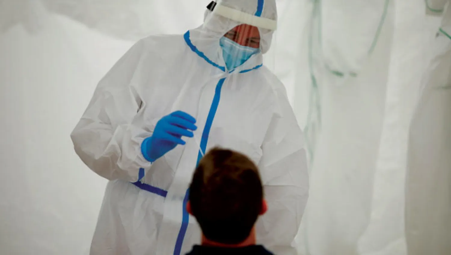 موظف طبي من الصليب الأحمر الألماني يجري فحصاً لكشف «كورونا» على مسافر بمحطة قطارات في برلين أمس (أ.ب)