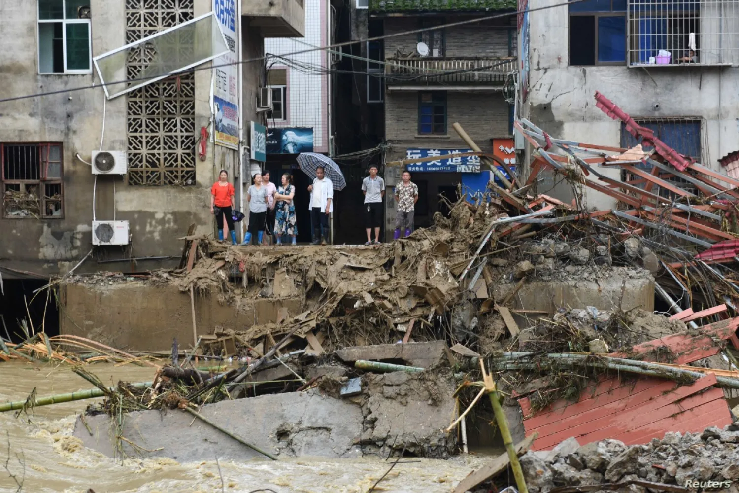 Residents stand on a bank of a river as they look at the rubble of a bridge damaged by flood following heavy rainfall in Nanjing, Fujian province, China, July 9, 2019. Reuters