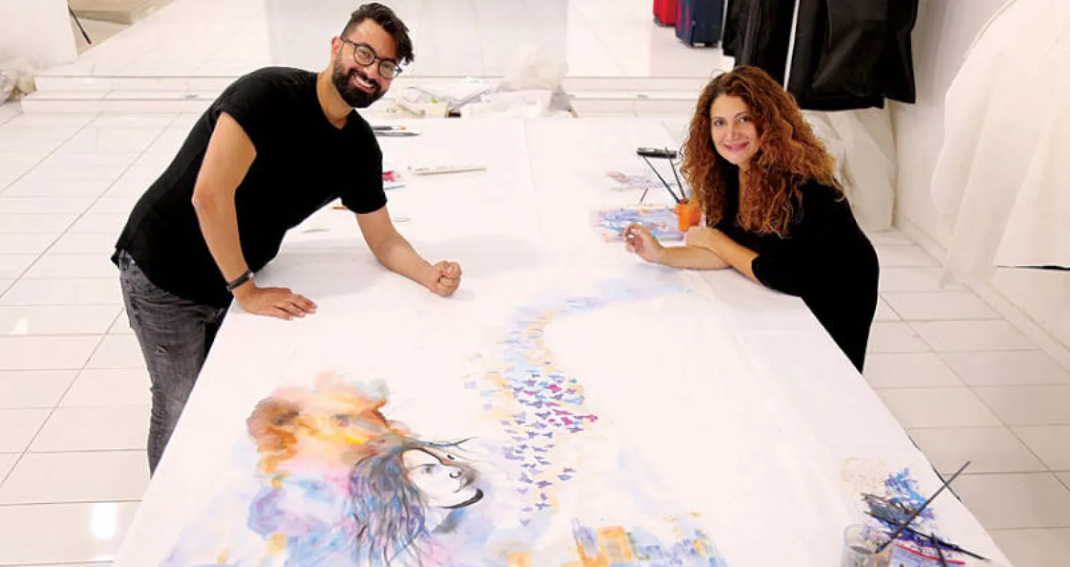 المصمم نجا سعادة والرسامة أدريانا الحاج خلال تنفيذهما فستان «أنا بيروت»