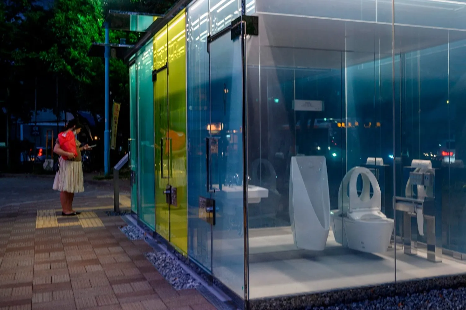 A woman stands in front of a transparent toilet designed by Shigeru Ban, at Haru-no-Ogawa Community Park in Tokyo, Japan on Aug. 19, 2020. (Getty Images)