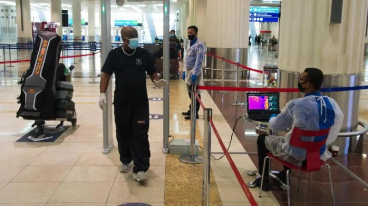 مسافر يرتدي قناعاً واقياً يمر خلال فحص درجة الحرارة في المبنى رقم 3 بمطار دبي الدولي (أ.ب)