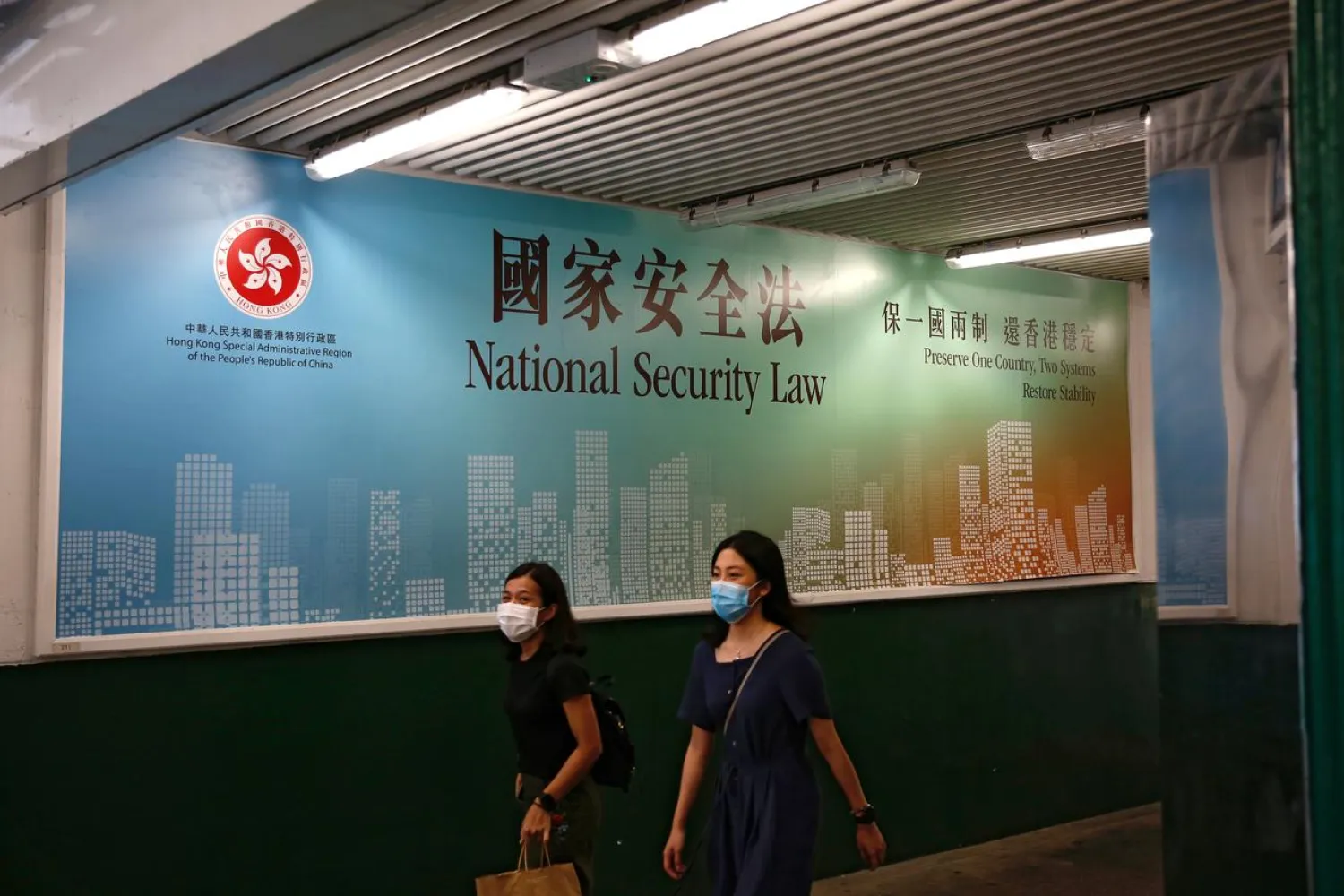 FILE PHOTO: Women walk past a government-sponsored advertisement promoting the new national security law as a meeting on national security legislation takes place in in Hong Kong, China June 29, 2020. REUTERS/Tyrone Siu