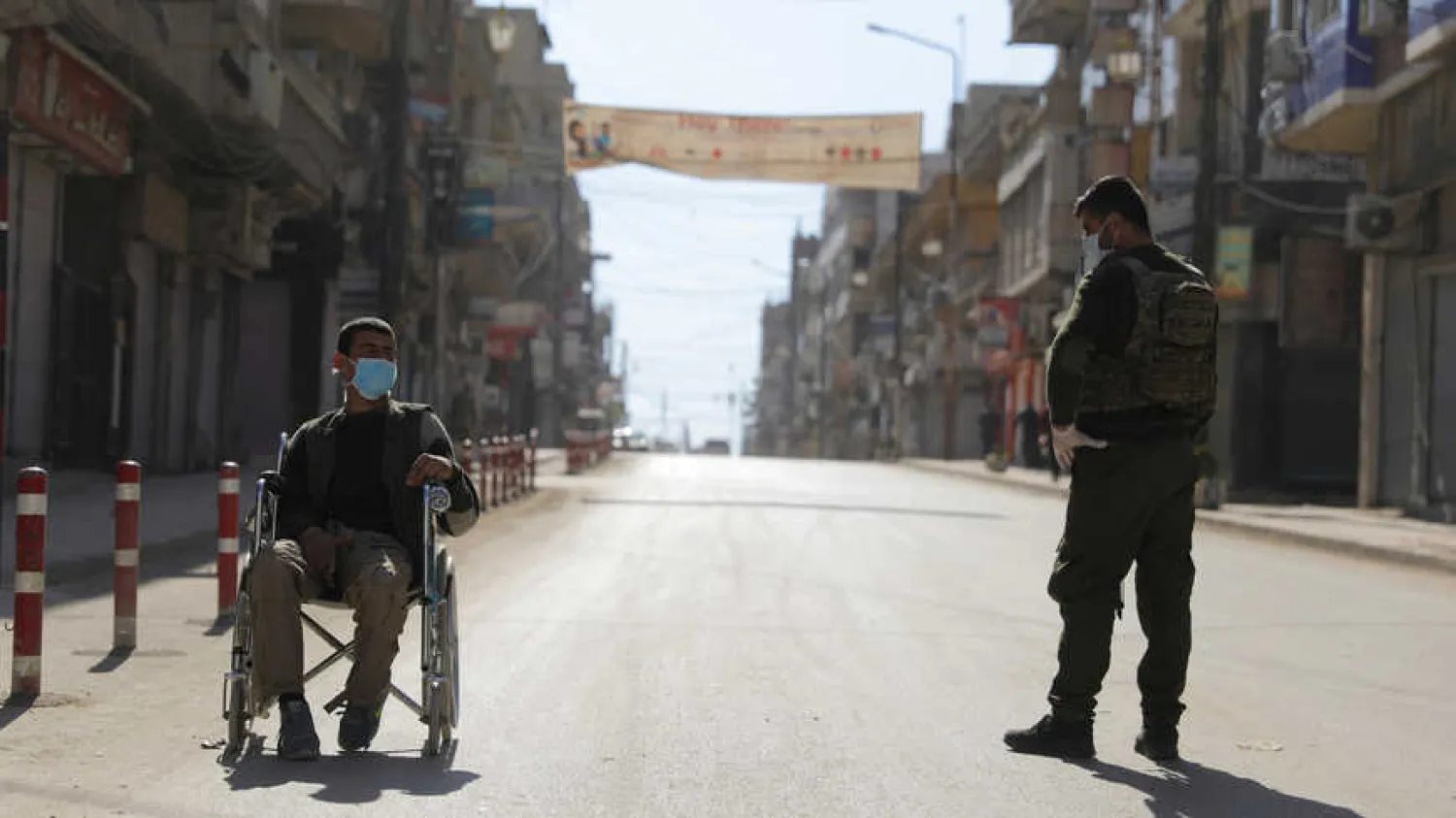 A member of the Kurdish-led security organization stands near a man in a wheelchair, as restrictions are imposed as measure to prevent the spread of the coronavirus disease in Qamishli, Syria (Reuters)