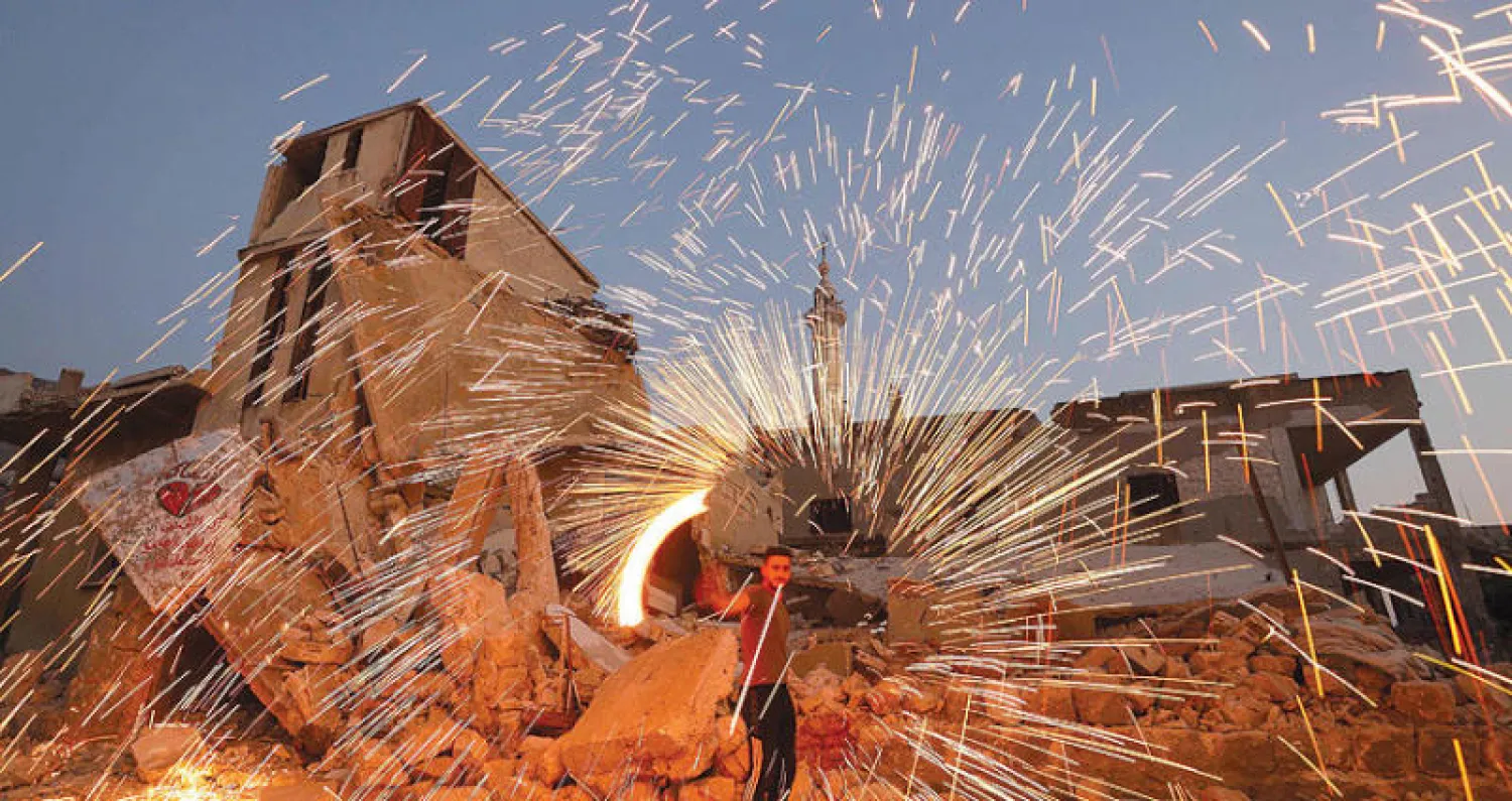 رجل يلفّ سلكاً معدنياً محترقاً وسط الأنقاض في بلدة آفس في إدلب (أ.ف.ب)