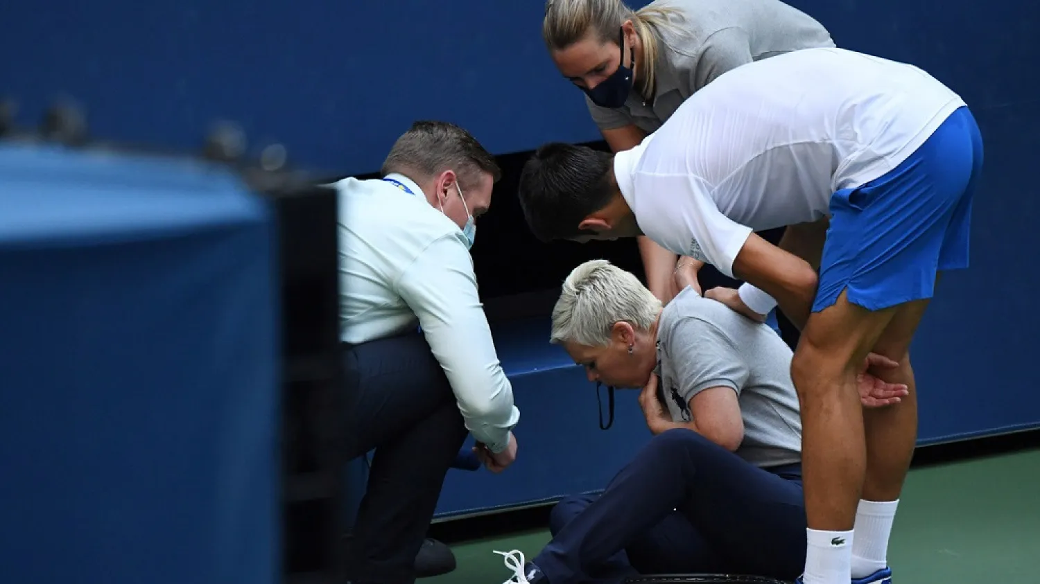Novak Djokovic of Serbia and a US Open tournament official tend to a linesperson who was struck with a ball by the Serb, Sept. 6, 2020. (Reuters)