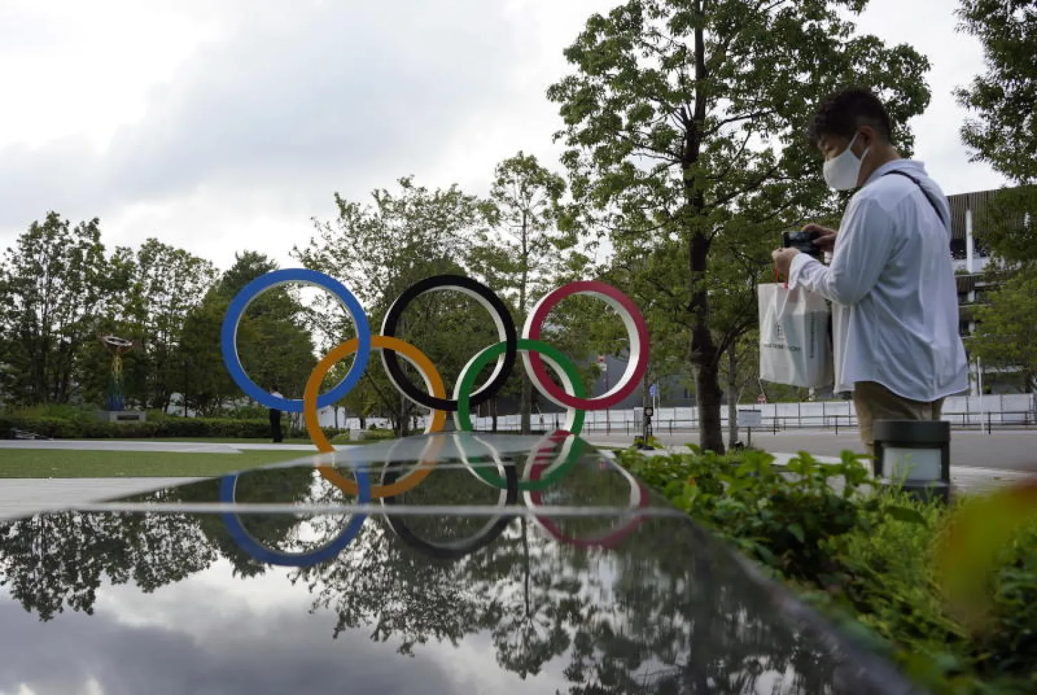 رجل يرتدي قناعاً واقياً يسير بجوار الشعار الأولمبي قرب الاستاد الوطني الذي يستضيف الألعاب في طوكيو (إ.ب.أ)
