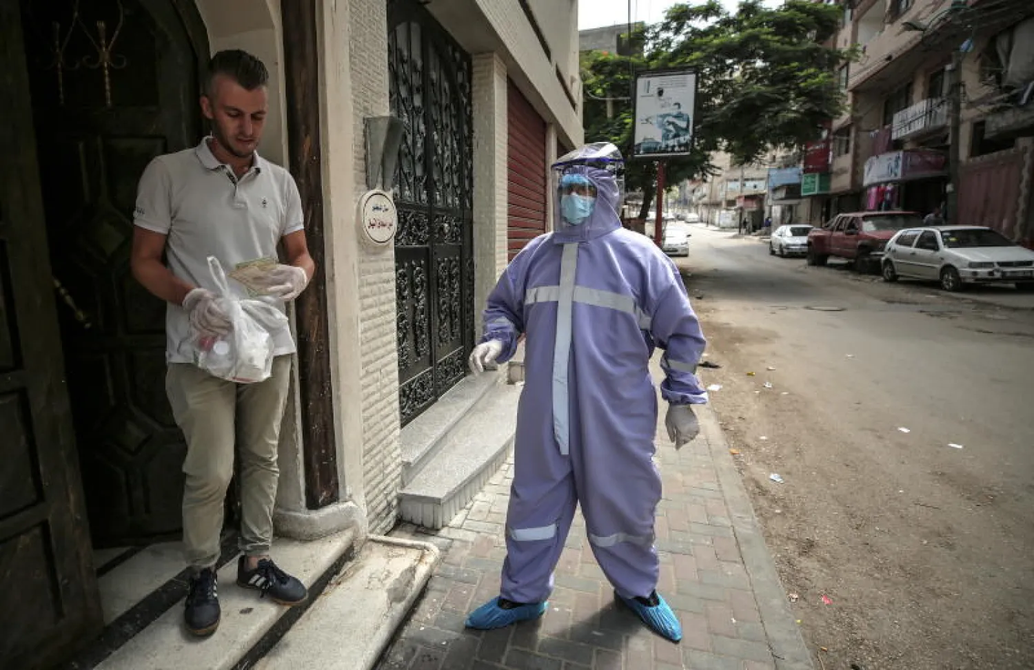 موظف في وكالة الأمم المتحدة لإغاثة وتشغيل لاجئي فلسطين (الأونروا) يرتدي ملابس واقية يوزع الأدوية على العائلات الفلسطينية في غزة (إ.ب.أ)