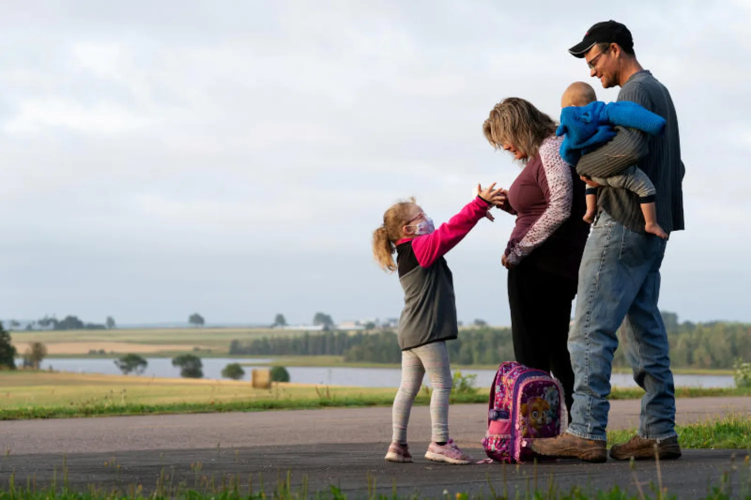 طفلة تنتظر الحافلة برفقة والديها مع إعادة فتح المدارس في كندا (رويترز)