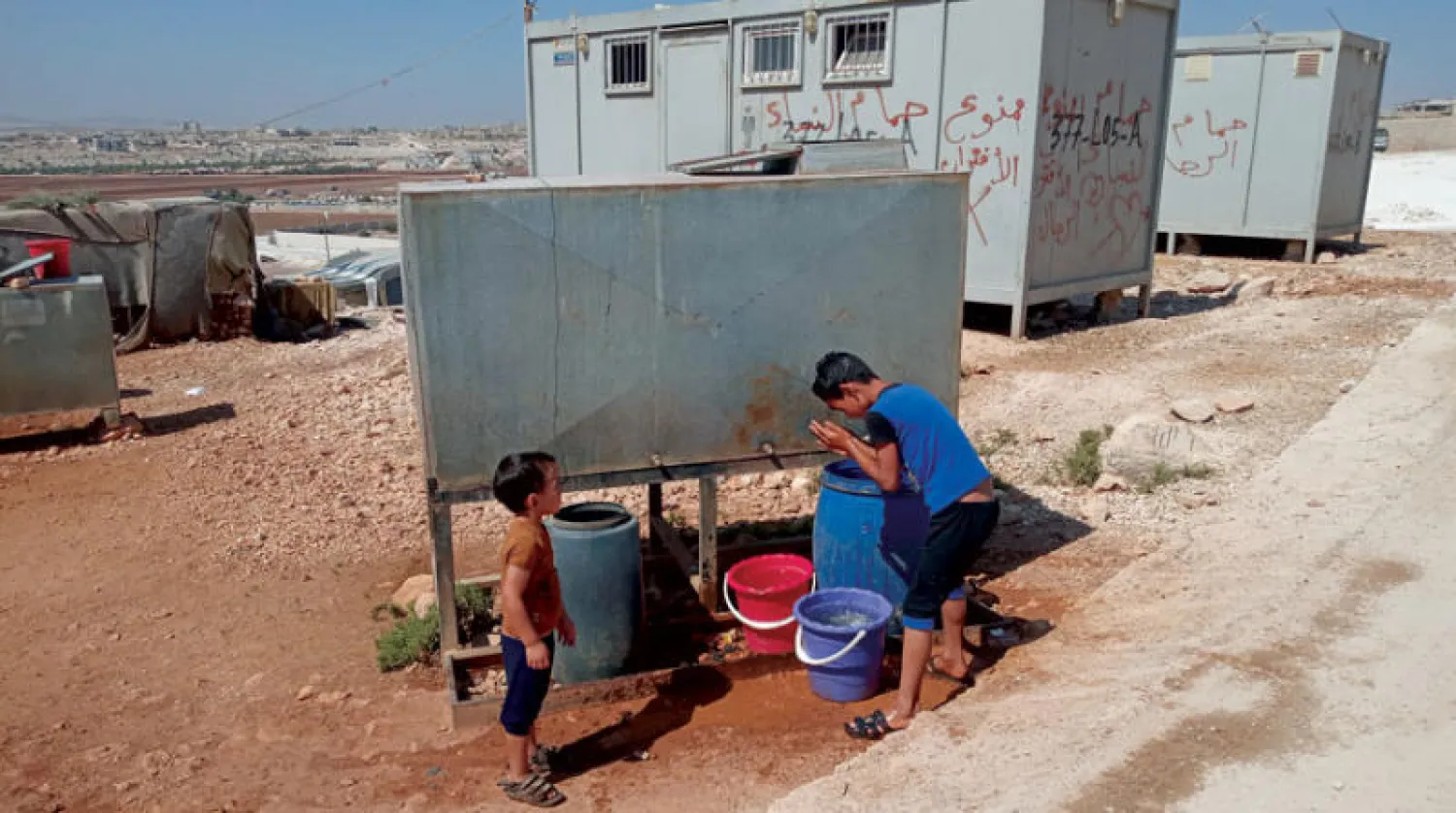 طفلان يلطفان من الحرارة بسكب المياه عليهما في ريف إدلب (الشرق الأوسط)