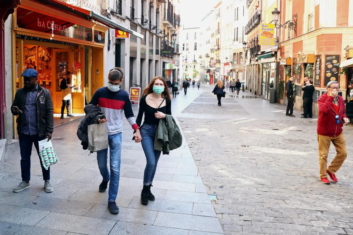 A couple wear protective face masks as they walk in unusually quiet Postas street in central Madrid, Spain, March 13, 2020. REUTERS/Sergio Perez