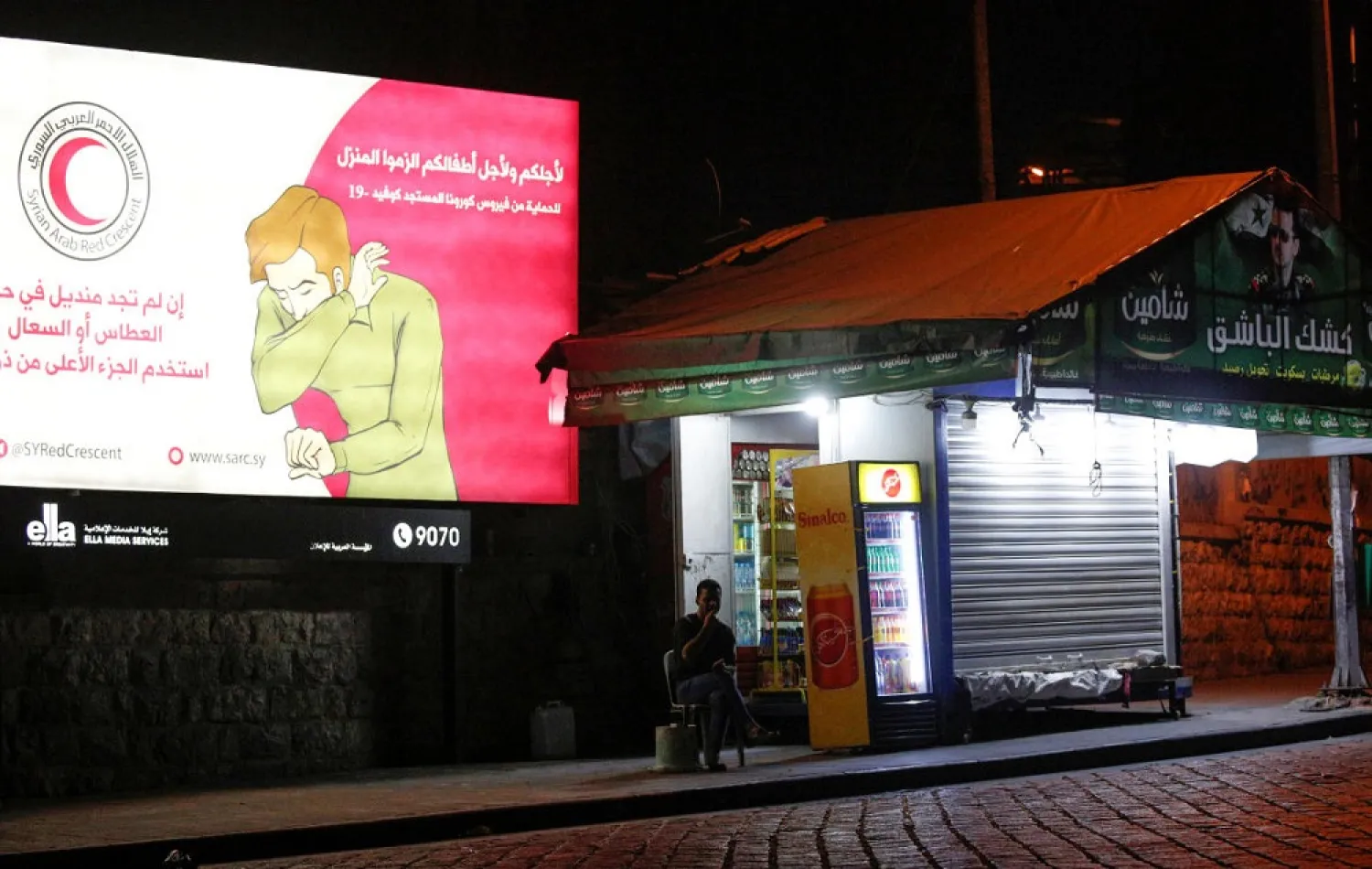 A man sits near a coronavirus awareness billboard, during a lockdown to prevent the spread of coronavirus disease (COVID-19), in Damascus, Syria, April 4, 2020. (Reuters)