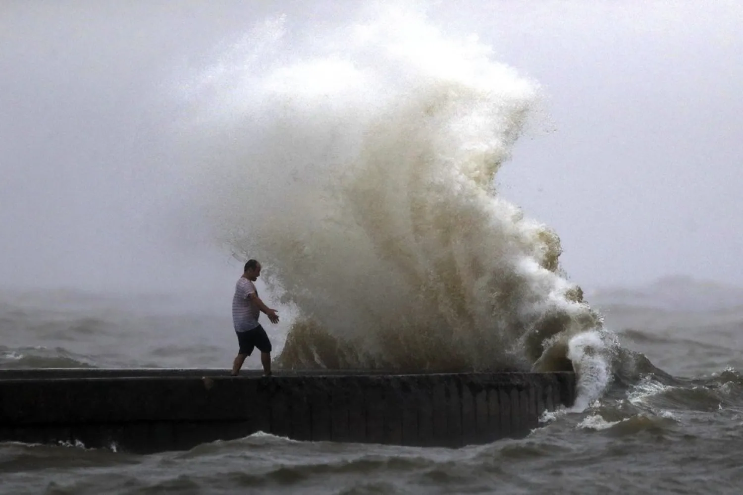 A wave crashes as a man stands on a jetty near Orleans Harbor in Lake Pontchartrain in New Orleans, Sunday, June 7, 2020, as Tropical Storm Cristobal approaches the Louisiana Coast. (AP)