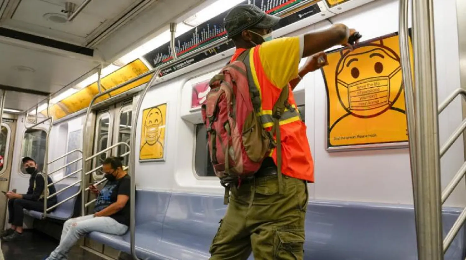 New York metrosunda bir görevli yolculara maske takılmasını hatırlatan afişler asıyor (AP)