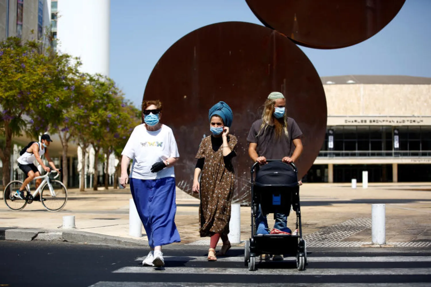 أشخاص يرتدون الكمامات في أحد شوارع تل أبيب (رويترز)