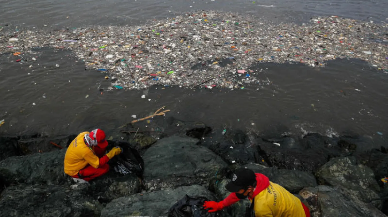 عمال يجمعون القمامة على شاطئ خليج مانيلا (إ.ب.أ)
