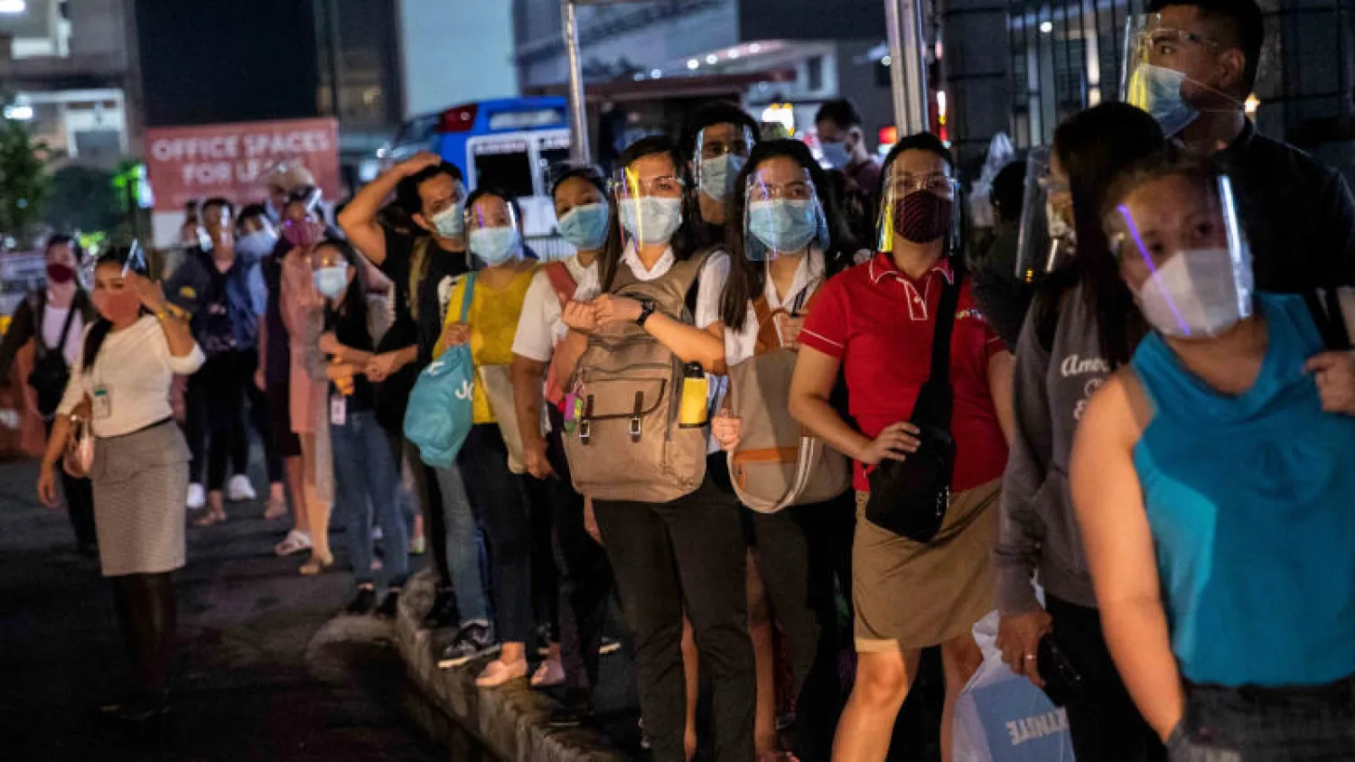 ركاب يرتدون أقنعة الوجه الواقية أثناء انتظارهم لإحدى الحافلات في مانيلا (رويترز)