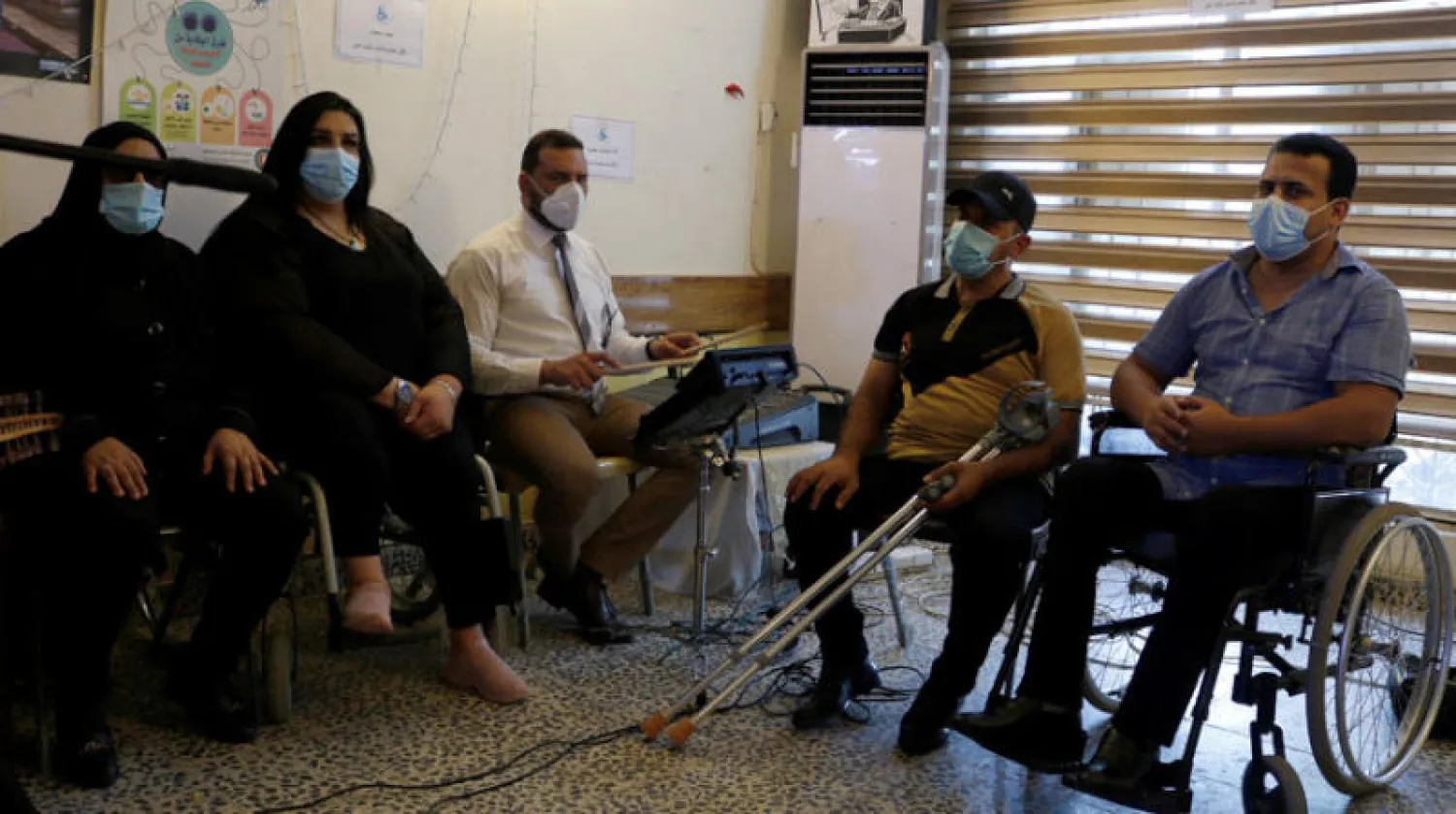 عراقيون يرتدون كمامات خلال الاستماع إلى ضرير يعزف على آلة موسيقية أمام أعضاء في تحالف المعوقين في بغداد في وقت سابق هذا الشهر (رويترز)