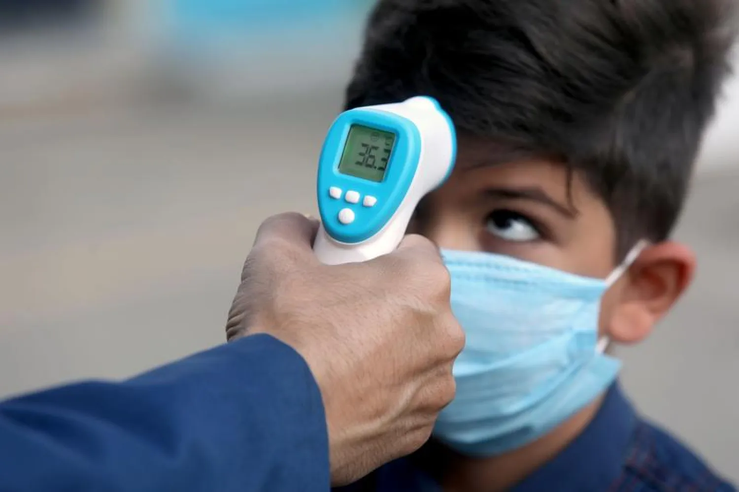 FILE PHOTO: A student wearing a protective face mask to help prevent the spread of the coronavirus disease (COVID-19), has his temperature taken by a school staff member at a school in Tehran. Reuters

