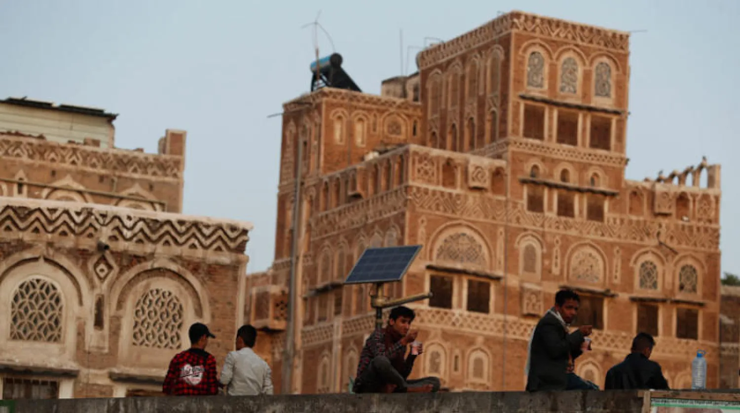 يمنيون يجلسون قرب سور مطل على مبان وسط صنعاء (إ.ب.أ)