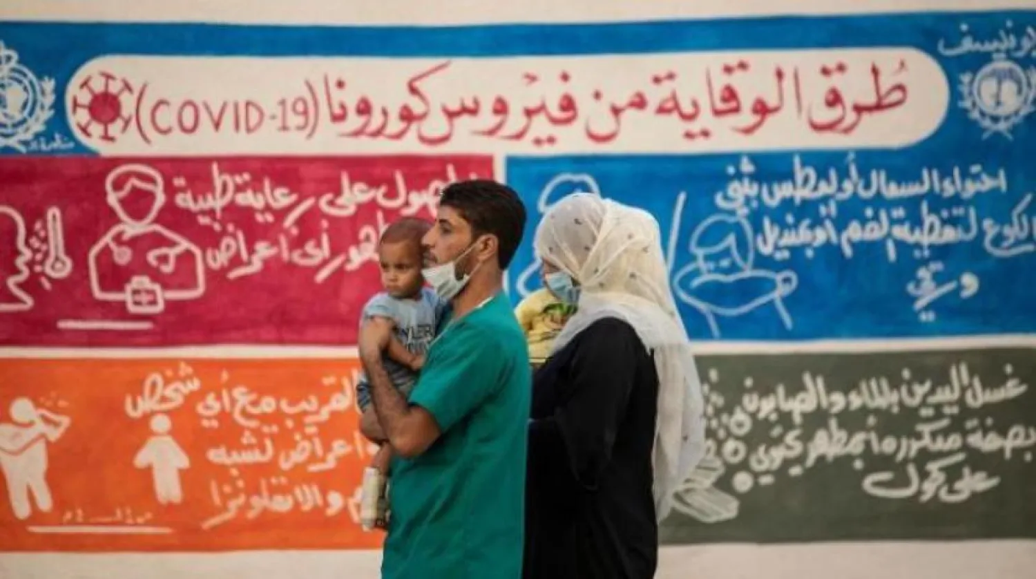 Suriyeli bir aile korona tedbirleri hakkındaki bir posterin önünde yürüyor (AFP)