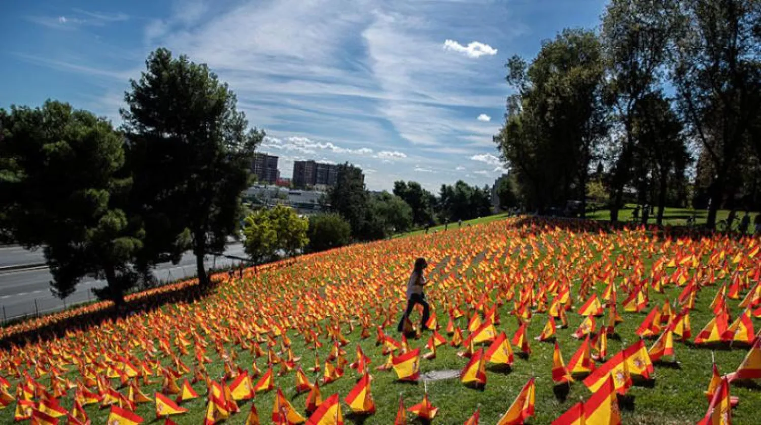 Madrid'de bir kadın Kovid-19 kurbanlarının anısına çimlere bırakılan İspanyol bayrakları arasında yürürken (AP) 