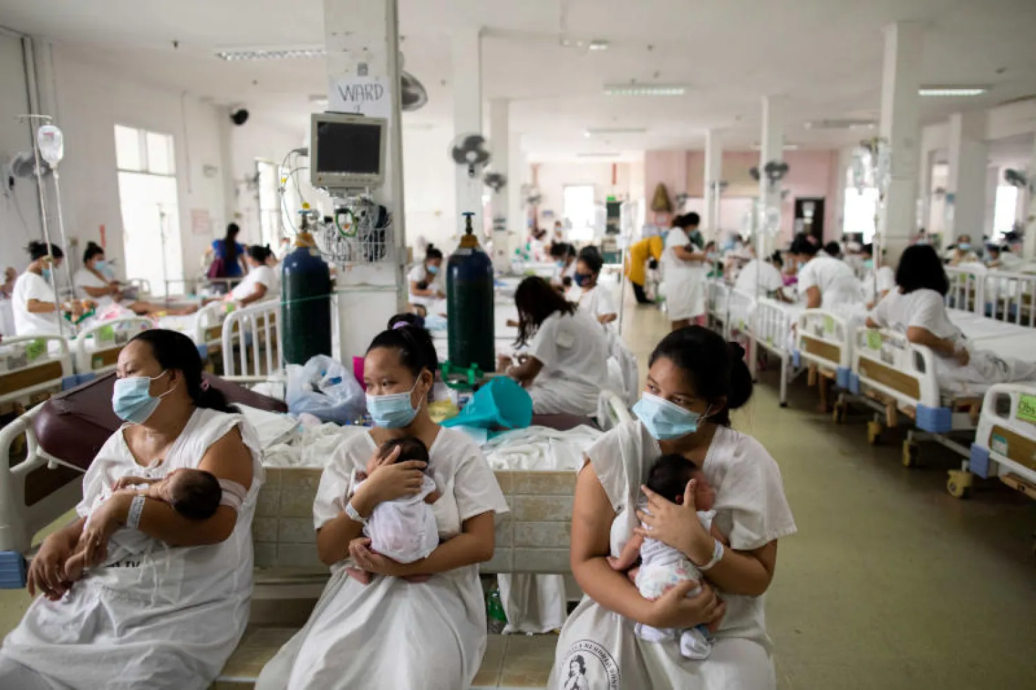 أمهات يحملن أطفالهن ويضعن الكمامات خوفاً من كورونا داخل مستشفى في الفلبين (رويترز)