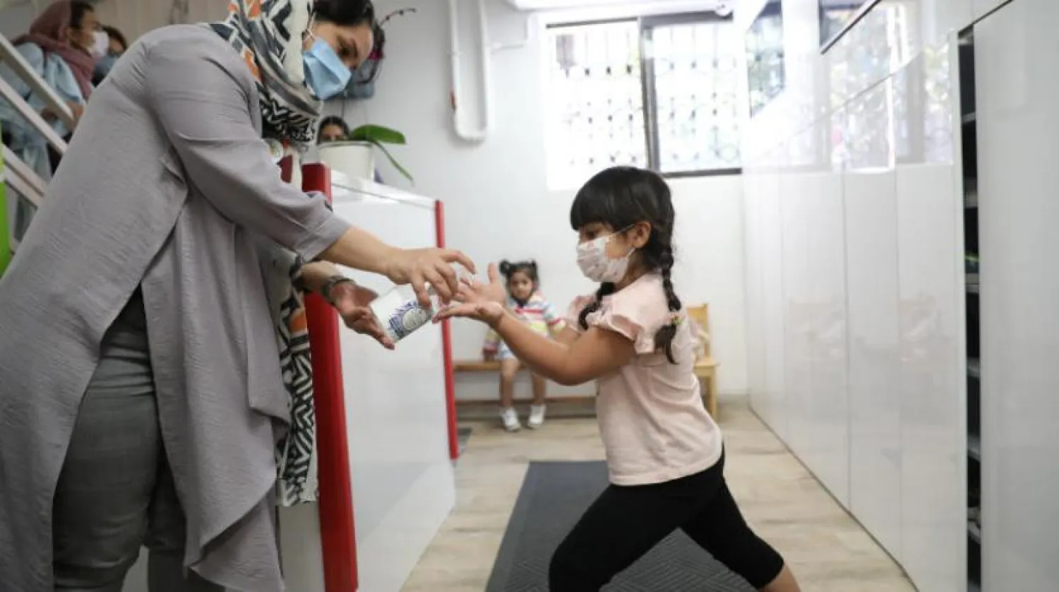 Tahran'da bir anaokulunda bir kız maske takıyor ve ellerini dezenfekte ediyor (Reuters)