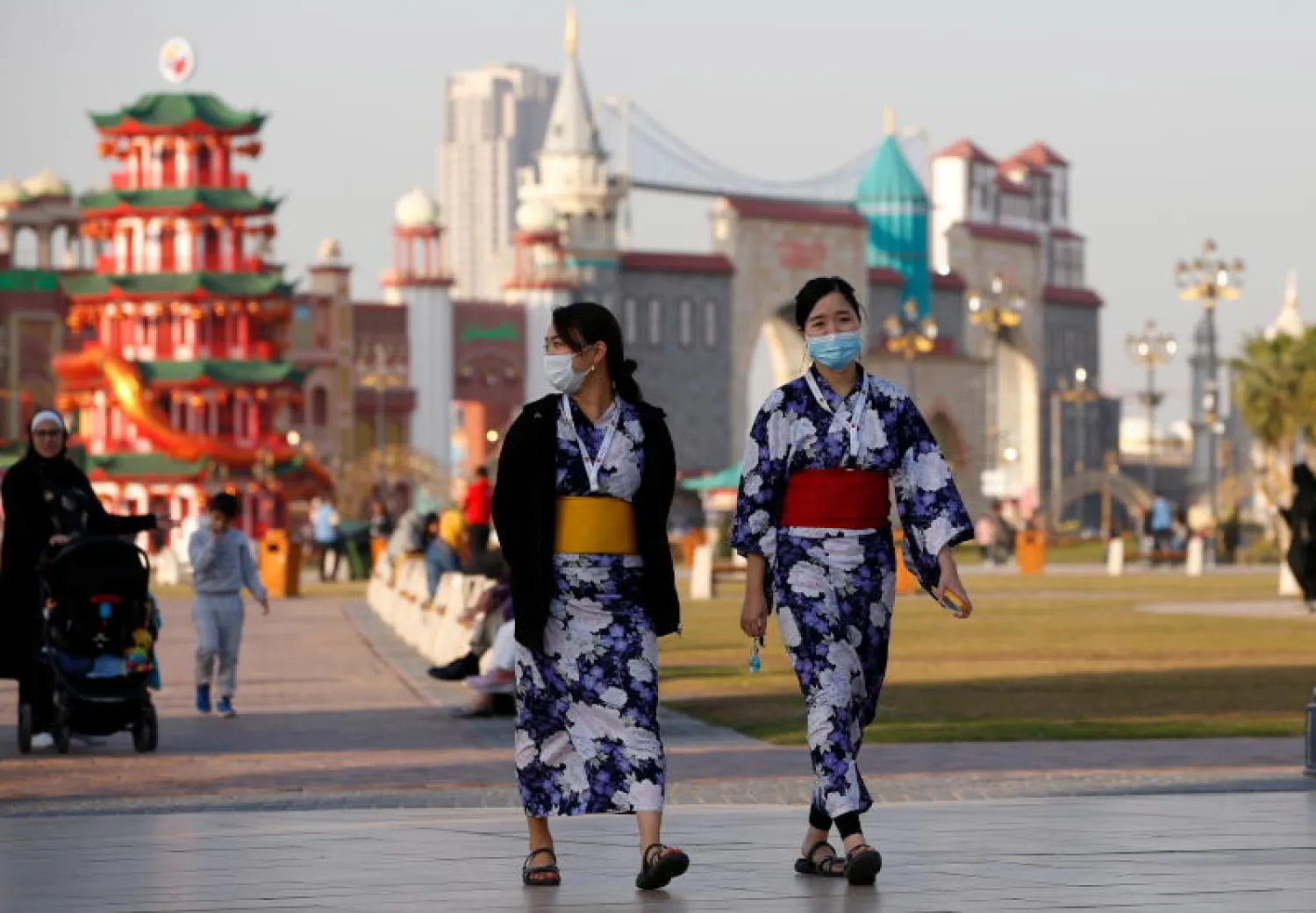 سائحتان آسيويتان تضعان قناعين واقيين وتتجولان بالقرية العالمية في دبي (إ.ب.أ)